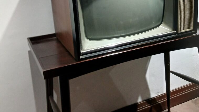 Un vieux téléviseur allumé dans une pièce sombre, évoquant une scène de série d'horreur des années 70 et 2020