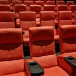 Salle de cinéma vide avec des rangées de fauteuils rouges sous une lumière tamisée