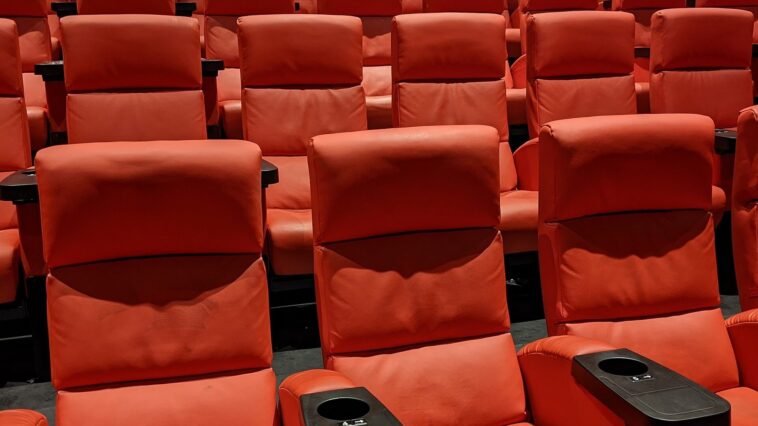 Salle de cinéma vide avec des rangées de fauteuils rouges sous une lumière tamisée