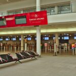 Comptoir d'enregistrement d'un aéroport avec des voyageurs et des valises, illustrant une règle bagages en cabine